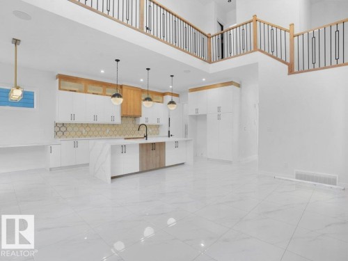 Kitchen with white cabinetry, decorative light fixtures, a towering ceiling, an island with sink, and light marble finish flooring - 6131 Crawford Drive, Edmonton, AB - Indoor Photo Showing Kitchen