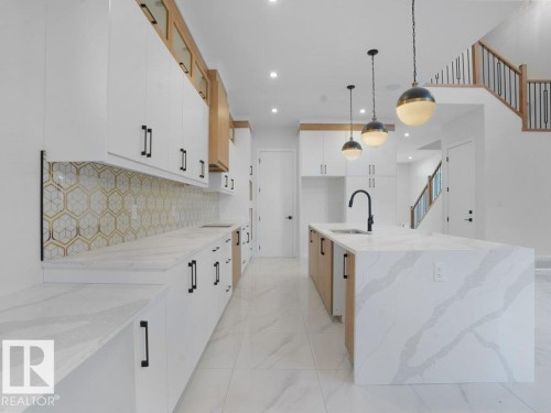 Kitchen with white cabinets, light stone counters, hanging light fixtures, an island with sink, and decorative backsplash - 6131 Crawford Drive, Edmonton, AB - Indoor