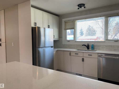 Kitchen featuring appliances with stainless steel finishes, white cabinets, light stone countertops, and tasteful backsplash - 10816 163 Street, Edmonton, AB - Indoor Photo Showing Kitchen