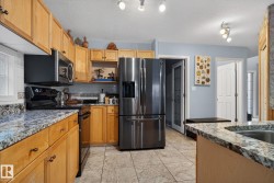 Kitchen featuring appliances with stainless steel finishes, light stone countertops, a textured ceiling, tasteful backsplash, and brown cabinetry - 