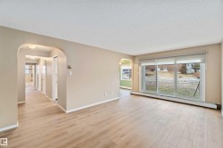 Empty room featuring light wood-type flooring, baseboard heating, arched walkways, and a textured ceiling - 