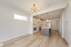 Kitchen featuring white cabinets, backsplash, a center island with sink, appliances with stainless steel finishes, and decorative light fixtures - 
