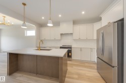 Kitchen featuring stainless steel appliances, decorative backsplash, white cabinets, an island with sink, and light wood-type flooring - 