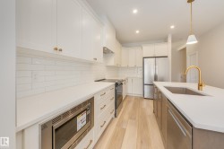 Kitchen with appliances with stainless steel finishes, white cabinetry, light wood-style flooring, backsplash, and pendant lighting - 