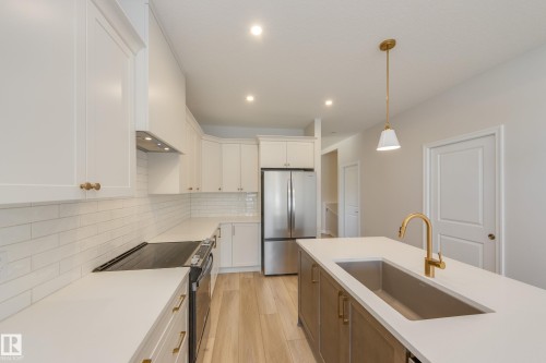 Kitchen with electric range oven, freestanding refrigerator, backsplash, hanging light fixtures, and light wood-style flooring - 199 Stonehouse Way, Leduc, AB - Indoor Photo Showing Kitchen With Upgraded Kitchen
