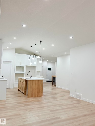 Kitchen with decorative light fixtures, an island with sink, open floor plan, lofted ceiling, and light wood-style flooring - 3320 Chickadee Drive, Edmonton, AB - Indoor Photo Showing Kitchen
