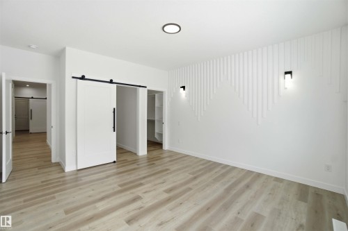 Unfurnished bedroom featuring a barn door, a spacious closet, and light wood-type flooring - 3320 Chickadee Drive, Edmonton, AB - Indoor Photo Showing Other Room