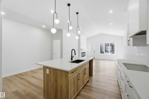 Kitchen with a kitchen island with sink, light wood finished floors, two tone cabinets, hanging light fixtures, and light stone countertops - 3320 Chickadee Drive, Edmonton, AB - Indoor Photo Showing Kitchen With Double Sink With Upgraded Kitchen