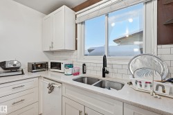 Kitchen featuring white cabinets, white appliances, light stone countertops, and tasteful backsplash - 