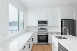 Kitchen featuring stainless steel appliances, backsplash, white cabinets, modern cabinets, and light wood-style floors - 