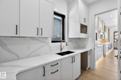 Kitchen featuring white cabinetry, light wood-type flooring, tasteful backsplash, and light stone counters - 