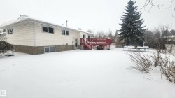 Snow covered back of property with a trampoline, a wooden deck, and stairs - 