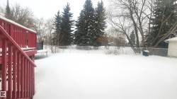 Yard covered in snow featuring a trampoline, a fenced backyard, and a deck - 