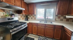 Kitchen featuring gas range, under cabinet range hood, decorative backsplash, and brown cabinets - 
