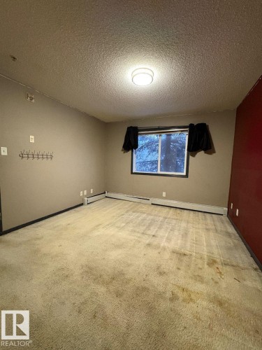 Spare room featuring light carpet, a textured ceiling, and a baseboard heating unit - 231 1180 Hyndman Road, Edmonton, AB - Indoor Photo Showing Other Room