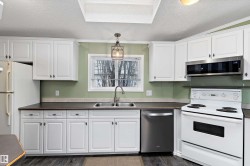 Kitchen featuring a textured ceiling, stainless steel appliances, white cabinetry, crown molding, and dark countertops - 