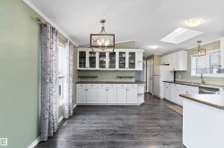 Kitchen with white cabinetry, a skylight, ornamental molding, dark wood-style flooring, and a chandelier - 