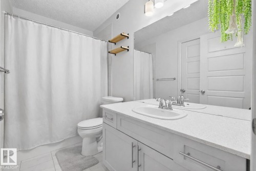 The bathroom features a vanity with a white countertop and an integrated sink, a toilet, and a shower area with a white curtain - 8 Daniel Street, Fort Saskatchewan, AB - Indoor Photo Showing Bathroom