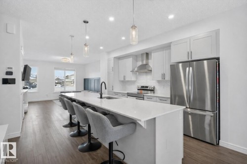 Open-concept kitchen with a large island, stainless steel appliances, light gray cabinetry, and hardwood floors - 8 Daniel Street, Fort Saskatchewan, AB - Indoor Photo Showing Kitchen With Stainless Steel Kitchen With Upgraded Kitchen