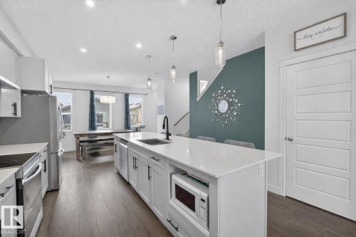 The kitchen features white cabinetry, stainless steel appliances, and a central island with a sink and pendant lighting - 8 Daniel Street, Fort Saskatchewan, AB - Indoor Photo Showing Kitchen With Upgraded Kitchen