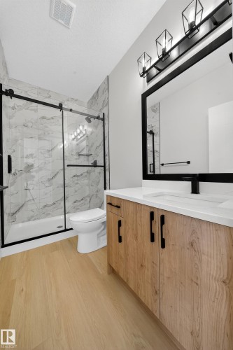 Bathroom with vanity, light wood-style floors, a marble finish shower, and a textured ceiling - 3285 Chernowski Way Sw, Edmonton, AB - Indoor Photo Showing Bathroom