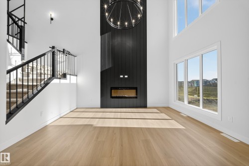 Unfurnished living room featuring stairs, a large fireplace, light wood finished floors, a towering ceiling, and plenty of natural light - 3285 Chernowski Way Sw, Edmonton, AB - Indoor Photo Showing Other Room With Fireplace