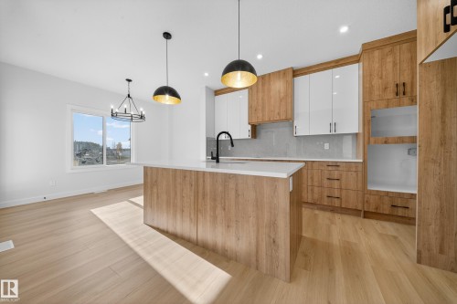 Kitchen with white cabinets, brown cabinets, decorative backsplash, decorative light fixtures, and a kitchen island with sink - 3285 Chernowski Way Sw, Edmonton, AB - Indoor Photo Showing Kitchen