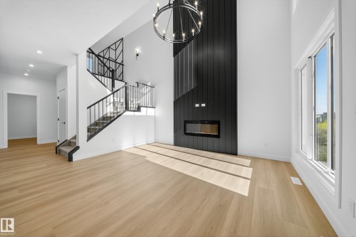 Unfurnished living room with a fireplace, light wood-type flooring, stairway, a high ceiling, and a chandelier - 3285 Chernowski Way Sw, Edmonton, AB - Indoor With Fireplace