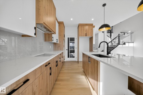 Kitchen featuring light stone countertops, pendant lighting, light wood-style floors, brown cabinets, and recessed lighting - 3285 Chernowski Way Sw, Edmonton, AB - Indoor Photo Showing Kitchen With Upgraded Kitchen