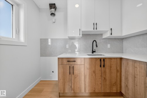 Kitchen featuring modern cabinets, white cabinets, light stone counters, backsplash, and light wood-style floors - 3285 Chernowski Way Sw, Edmonton, AB - Indoor Photo Showing Kitchen