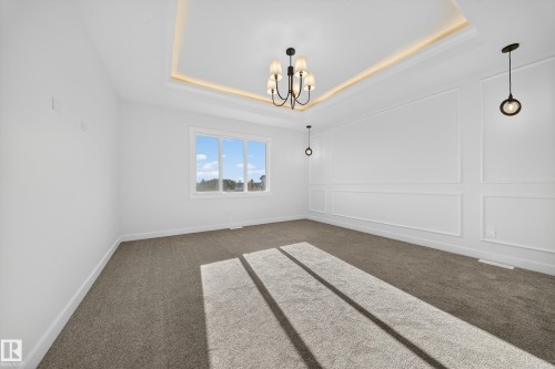 Carpeted spare room with a decorative wall, a tray ceiling, and a chandelier - 3285 Chernowski Way Sw, Edmonton, AB - Indoor Photo Showing Other Room