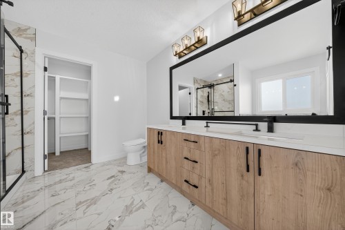 Full bath with a marble finish shower, light marble finish flooring, a walk in closet, and double vanity - 3285 Chernowski Way Sw, Edmonton, AB - Indoor Photo Showing Bathroom