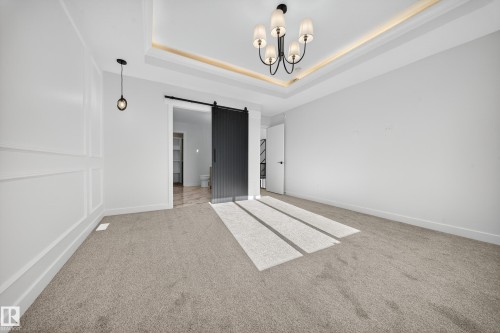 Carpeted spare room with a barn door, a chandelier, and a raised ceiling - 3285 Chernowski Way Sw, Edmonton, AB - Indoor Photo Showing Other Room