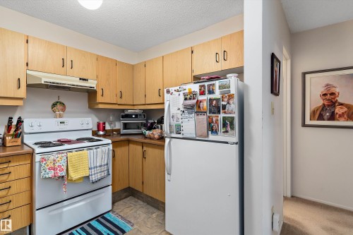 Kitchen with white appliances, under cabinet range hood, and a textured ceiling - 305 32 Alpine Place, St. Albert, AB - Indoor Photo Showing Kitchen