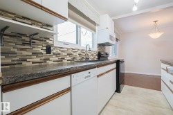 Kitchen featuring white appliances, white cabinetry, dark countertops, and hanging light fixtures - 