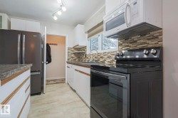 Kitchen with white appliances, dark countertops, white cabinets, tasteful backsplash, and light wood finished floors - 