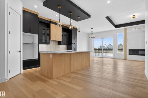 Open concept living space featuring light wood flooring, a kitchen island with a light-colored countertop, and a fireplace with a light-colored surround - 27 Rosewood Way, St. Albert, AB - Indoor Photo Showing Kitchen
