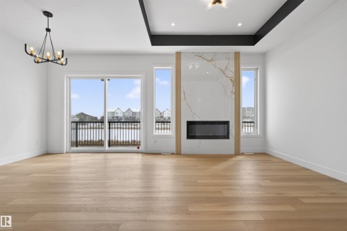 Living area featuring hardwood floors, a contemporary fireplace with a marble-effect surround, and large windows with a glass sliding door opening to a balcony - 27 Rosewood Way, St. Albert, AB - Indoor Photo Showing Living Room With Fireplace