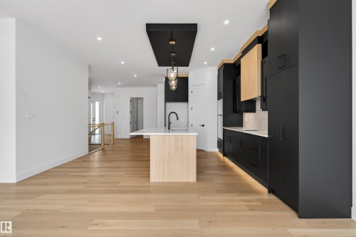 The kitchen features an island with a light wood base and white countertop, a black faucet, and a black ceiling-mounted light fixture with glass shades - 27 Rosewood Way, St. Albert, AB - Indoor
