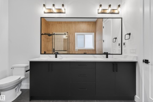 The bathroom features a dual vanity with a white countertop, two matte black faucets, and a large mirror - 27 Rosewood Way, St. Albert, AB - Indoor Photo Showing Bathroom