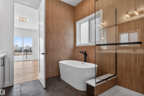 The bathroom features a freestanding tub, a glass-enclosed shower with a bench, and a window for natural light - 27 Rosewood Way, St. Albert, AB - Indoor Photo Showing Bathroom