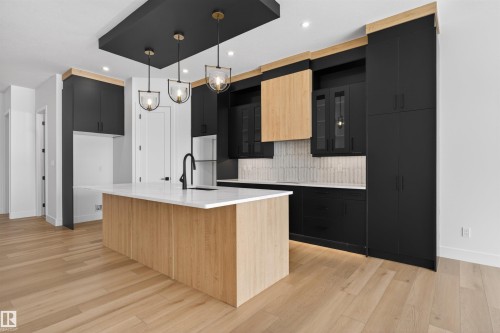 The kitchen features light wood flooring and a central island with a white countertop and a black faucet - 27 Rosewood Way, St. Albert, AB - Indoor Photo Showing Kitchen