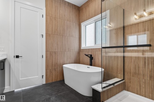 Bathroom featuring a freestanding bathtub with a black faucet, a glass-enclosed shower, wood-look wall tiles, and dark floor tiles - 27 Rosewood Way, St. Albert, AB - Indoor Photo Showing Bathroom