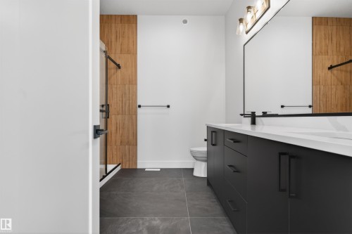 The bathroom features a dual vanity with a white countertop and dark cabinetry, a spacious mirror with overhead lighting, a toilet, and a shower with a clear glass enclosure - 27 Rosewood Way, St. Albert, AB - Indoor Photo Showing Bathroom