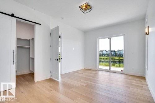Unfurnished bedroom with a barn door, a walk in closet, access to outside, and light wood finished floors - 27 Rosewood Way, St. Albert, AB - Indoor