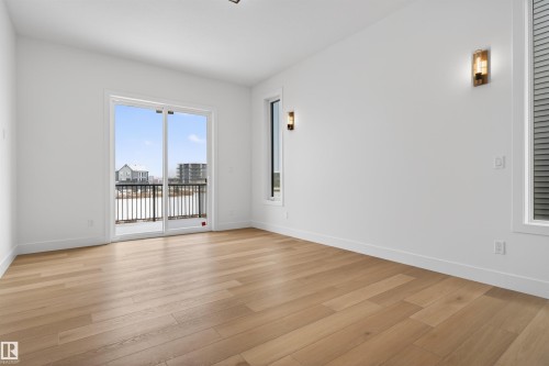 This bright room features light-toned hardwood flooring and a large sliding glass door opening to a balcony with black railings - 27 Rosewood Way, St. Albert, AB - Indoor