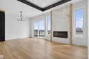 Spacious room featuring light wood flooring, a fireplace with a decorative stone surround, and large windows providing views of the exterior - 27 Rosewood Way, St. Albert, AB  - Indoor Photo Showing Living Room With Fireplace 