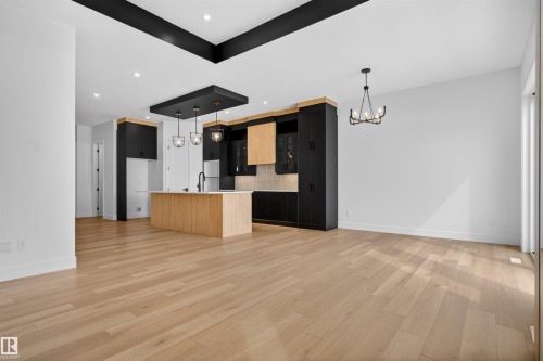 The property features light-toned hardwood flooring throughout, an open-concept kitchen with a light wood island, and dark cabinetry with light wood accents - 27 Rosewood Way, St. Albert, AB - Indoor Photo Showing Kitchen