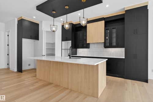 The kitchen features a spacious island with a light wood finish and a white countertop, complemented by dark cabinetry and a light-colored backsplash - 27 Rosewood Way, St. Albert, AB - Indoor Photo Showing Kitchen