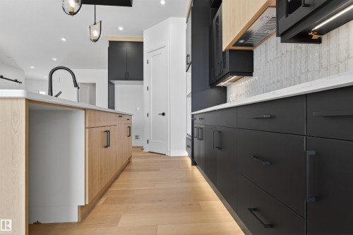 The property features a kitchen with light wood flooring, a central island with natural wood cabinetry, and a black faucet - 27 Rosewood Way, St. Albert, AB - Indoor